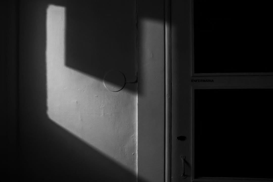 Luz de janela projetada numa parede junto a uma porta com a palavra Enfermaria